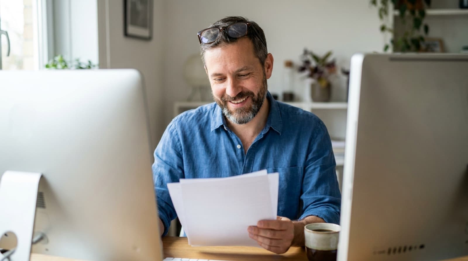 An accountant reviewing papers at a desk between two monitors, a coffee within reach